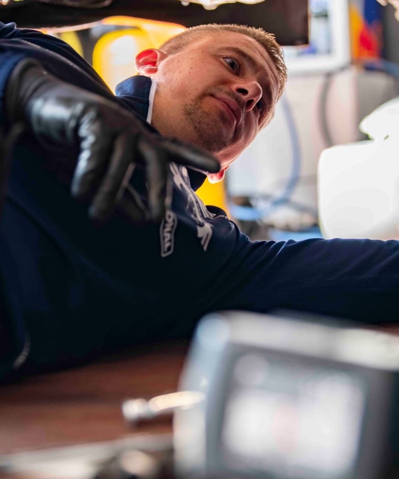 Bjorn Peeters aan het werk onder een wagen in de werkplaats
